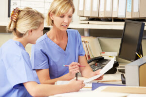 A Medical Assistant and a Certified Nursing Assistant going over charts at a medical office desk